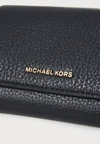 Juodas odinis piniginė su tekstūruota paviršiumi, su auksiniu "MICHAEL KORS" logotipu ir horizontaliu siuvimo detalumu.