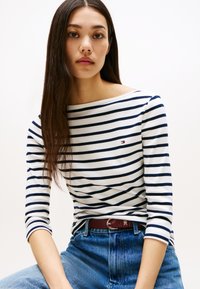 Baltas ir tamsiai mėlynas dryžuotas ilgomis rankovėmis viršus su valtine apykakle. Derinama su aukšto liemens mėlynais džinsais ir bordo spalvos diržu.