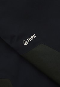 Zwarte stof met textuuraccenten in het groen, met een witte geborduurde branding "HIPE" en een waterdruppel logo aan de linkerkant.