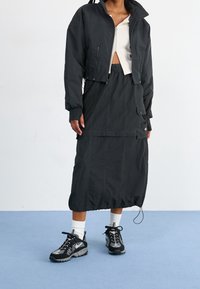 Svart kort jacka med dragkedja, ihop med en svart kjol med fickor och dragsko i nederkant. Skor: svarta och vita sneakers.