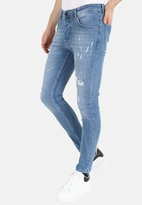 Blauwe denim skinny jeans met een versleten ontwerp met scheuren en vervaagde gebieden, zijzakken en een ritsluiting. Gepaard met witte sneakers.