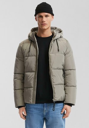 Gevoerde hoodie-jas in lichtgrijs, met een rits aan de voorkant, capuchon met trekkoord en zijzakken. Draagt over een zwarte trui en blauwe jeans.