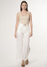 Beige glinsterend tanktop en witte wijde broek met een gouden riemgesp. Tan platform schoenen. Gladde textuur.
