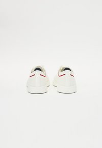 Sneaker bianchi con tessuto testurizzato, sottili accenti rossi sul tallone e suole in gomma. Il design presenta una forma a taglio basso per un look casual.