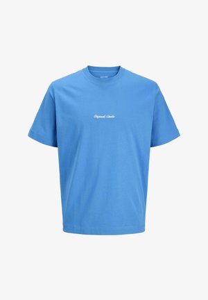 Έφηβος αγόρι με ανοιχτό μπλε τζιν, μπλε μπλουζάκι, μπλε σκούρο φούτερ με κουκούλα και μπεζ παπούτσια, στέκεται μπροστά σε απλό ανοιχτό φόντο, κοιτώντας δεξιά.