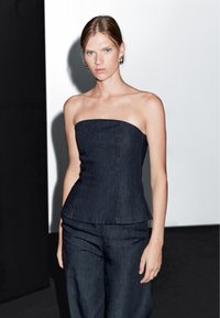 Bezramenný denimový top v tmavě námořnické barvě s přiléhavým siluetem a strukturovaným živůtkem. Prošívání zvýrazňuje tvar. Spárovaný s odpovídajícími kalhotami.