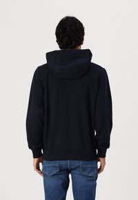 Sudadera azul marino hecha de tela suave, con una gran capucha, puños acanalados y un corte relajado. Combinada con jeans de mezclilla azules.