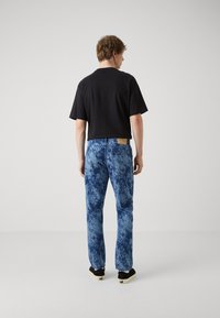 Camisa negra de manga corta combinada con jeans azul tie-dye, con corte recto, textura ligera y un parche de cuero beige en la cintura.