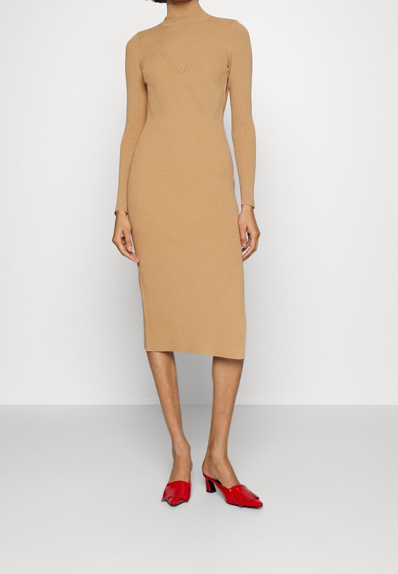 Abito midi in maglia marrone a maniche lunghe con collo alto e texture a motivo X. Abbinato a mule con tacco a blocco rossi.