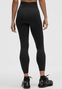 Leggings neri a vita alta realizzati in tessuto elastico, con una texture liscia e un logo sul retro. Adatti per l'abbigliamento sportivo.