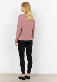 Roze gebreide langemouwtop met een ronde hals, gecombineerd met strakke zwarte jeans en zwarte platte schoenen. Eenvoudig ontwerp met een zachte textuur.