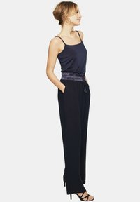 Granatowy kombinezon z wąskimi ramiączkami, elastyczną talią i bocznymi kieszeniami. Wykonany z miękkiego materiału w luźnym kroju, uzupełniony o sandały na obcasie.