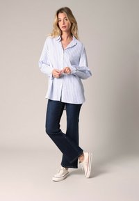 Gestreepte overhemd in lichtblauw en wit, gecombineerd met donkere spijkerbroek met flair en witte sneakers. Het shirt heeft lange mouwen en een ontspannen pasvorm.