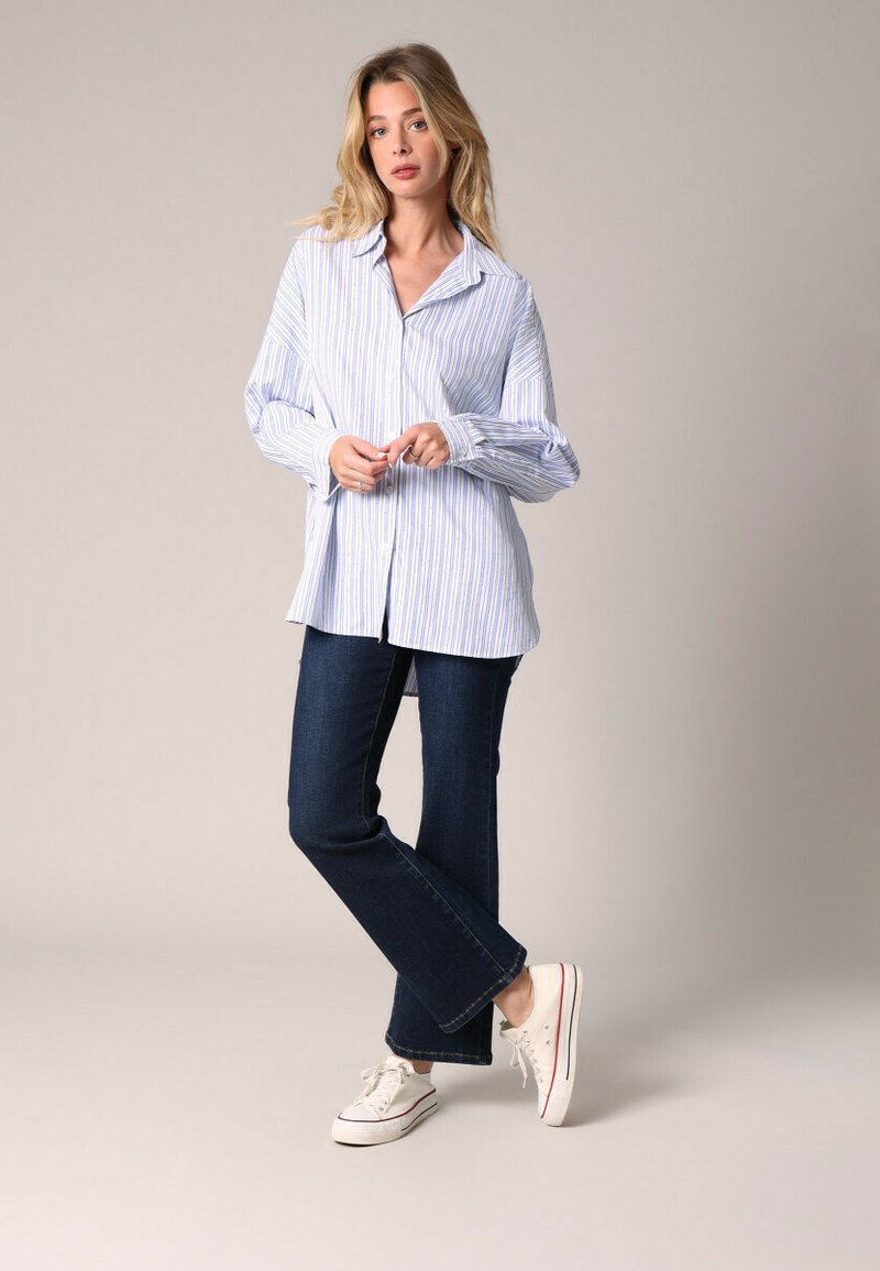 Gestreepte overhemd in lichtblauw en wit, gecombineerd met donkere spijkerbroek met flair en witte sneakers. Het shirt heeft lange mouwen en een ontspannen pasvorm.