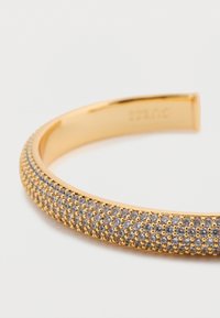 Βραχιόλι σε χρυσό τόνο με υφή στην επιφάνεια και συστάδες από διαυγή πετράδια, λεία εσωτερική επιφάνεια και διακριτική σήμανση στη πλευρά.