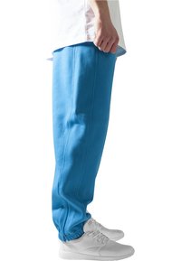 Pantaloni de trening de un albastru deschis, fabricați dintr-un material moale, cu un design ajustat, manșete elastice și cusături laterale. Asortați cu pantofi sport albi.