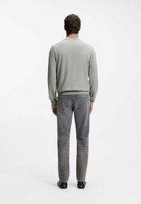 Szary sweter typu pulower z okrągłym dekoltem i długimi rękawami w zestawieniu z szarymi jeansami o prostym kroju i tylnych kieszeniach.