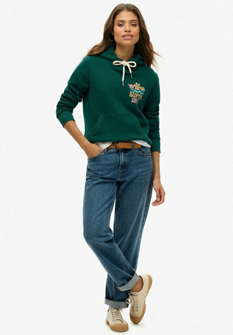 Groene hoodie met koordjes en bloemenborduurwerk, gecombineerd met opgerolde blauwe jeans en beige sneakers. Casual ontwerp met een voorzak.