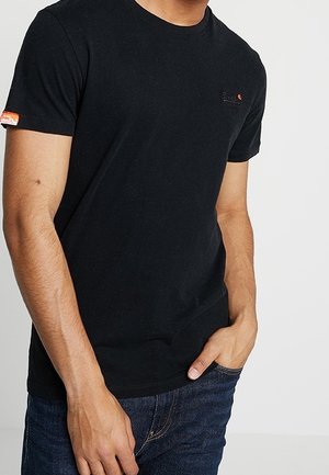 Sort bomulds t-shirt med rund hals, tætsiddende design og lille logo på brystet. Båret sammen med mørkeblå denim jeans.