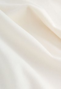 Tessuto di cotone in un bianco crema morbido, con una texture liscia e leggermente elastica, che mostra una sottile costina e pieghe delicate.