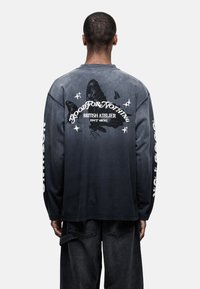 Maglietta a maniche lunghe con sfumatura da nero a grigio, caratterizzata da una grande grafica di farfalla e testo sul retro, con accenti di testo bianco a contrasto.