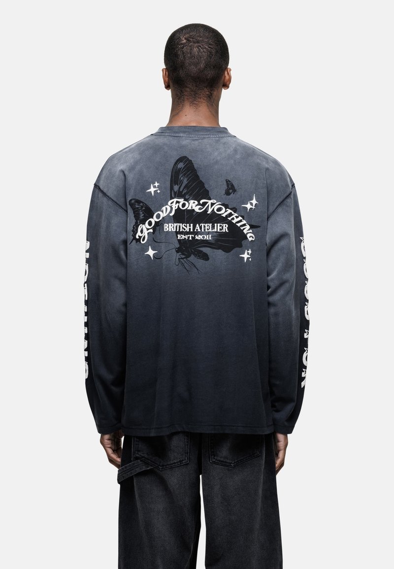 Maglietta a maniche lunghe con sfumatura da nero a grigio, caratterizzata da una grande grafica di farfalla e testo sul retro, con accenti di testo bianco a contrasto.