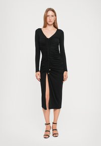 Black, long-sleeve dress with gathered texture, V-neck, front slit, and gold button accents, made from a smooth, stretchy fabric.