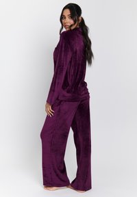 Samling av lyxiga loungewear i djup lila, med en långärmad topp och lösa byxor med en mjuk textur och avslappnad passform, utan synliga mönster.