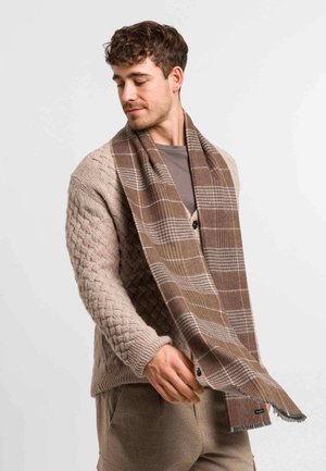 Cárdigan de punto beige con un patrón de trenza texturizada, combinado con una bufanda de cuadros marrón que presenta bordes deshilachados y un sutil detalle de logotipo.