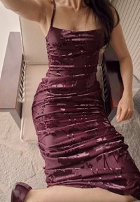 Bordeaux jurk met dunne bandjes, gerimpelde textuur, bloemenpatroon en knie-lange lengte. Draagt met bijpassende bordeaux schoenen.