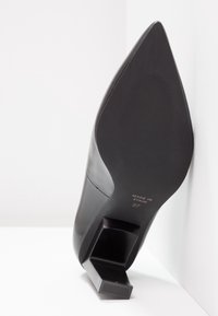Chaussure noire à talon haut avec un bout pointu et un talon carré, en cuir lisse. Présente un logo embossé et la taille 37 sur la semelle.