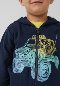 Marineblauer Zip-Hoodie mit einem Grafikdesign eines Geländewagens in Gelb und Türkis. Weicher Stoff, Frontreißverschluss und eine Kängurutasche.