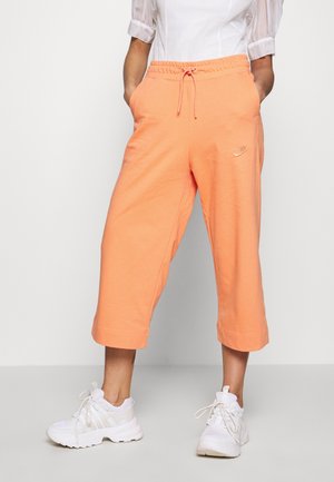 Spodnie dresowe Nike w jasnym brzoskwiniowym kolorze, wykonane z miękkiego materiału, z elastycznym pasem w talii i ściągaczem, o długości 7/8. Małe logo na biodrze.