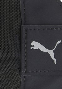 Patch en matériau noir arborant le logo argenté de Puma. La surface est lisse avec des détails de couture autour des bords.