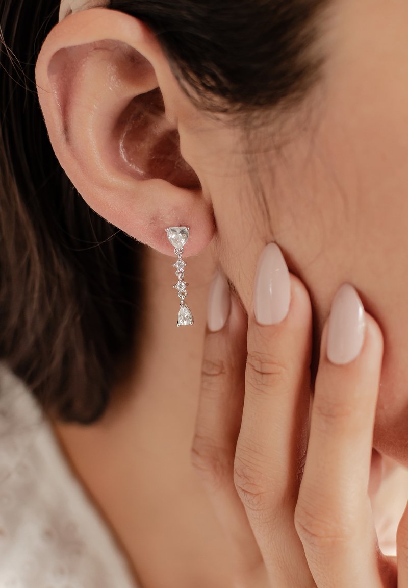 Pendientes de gota de plata con piedras transparentes en forma de pera y redondas, colgando de delicadas cadenas. Acabado suave y pulido; diseño elegante.