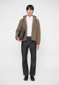 Rjav zip-up jakna, bela srajca, temno siva krojena hlače in črne čevlje. Drži črn aktovko. Preprost, sodoben dizajn.