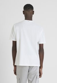 T-shirt bianca in cotone con collo giro, maniche corte e orlo dritto. Presenta un design minimalista senza motivi visibili.