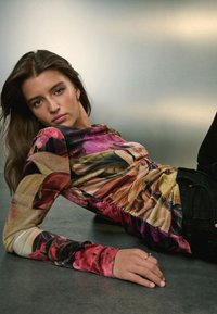 Langärmliges Oberteil mit Blumenmuster in den Farben Pink, Lila und Grün, mit Raffungen, kombiniert mit schwarzer Hose.