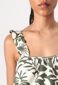 Žalios ir kreminės spalvos gėlių rašo tank topas, su raukšlėmis ant petnešų, kvadratine iškirptė ir lengvu audiniu.