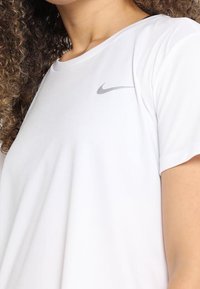 Camiseta blanca de Nike con cuello redondo, mangas cortas y un logo gris sutil en la parte superior izquierda. Textura suave, ajuste casual.