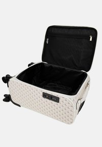 Valise rigide blanche avec un motif géométrique, intérieur noir, poche en maille interne et serrure à combinaison. Roues rétractables incluses.