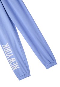Pantaloni della tuta azzurro chiaro con polsini elasticizzati, con la scritta "NEW YORK" stampata in bianco lungo la gamba sinistra. Tessuto morbido e design comodo.