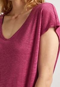 Top a maniche corte di colore lampone con scollatura a V. Il tessuto appare leggero e con texture, con una vestibilità ampia attorno alle spalle.