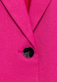 Fuchsia blazer med skarpt revers, tekstureret stof og en blank sort knap med to huller, der fremhæver en skræddersyet pasform.