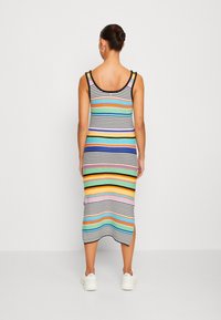 Robe maxi rayée avec un mélange de couleurs vives et des accents noirs, design sans manches, avec des fentes latérales. Fabriquée en tissu maille côtelée.