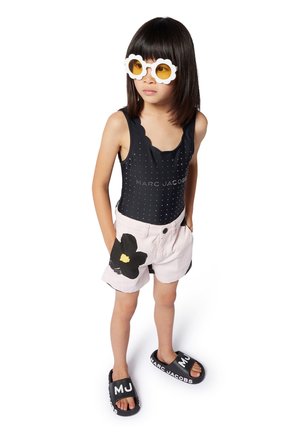 Maillot de bain noir à pois avec des bords festonnés, shorts rose clair ornés d'un imprimé de fleurs noires, et sandales noires avec texte blanc.