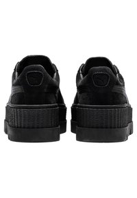 Une paire de baskets plateformes en suede noir vue de l'arrière, présentant des semelles épaisses texturées et le logo Puma sur la languette du talon.