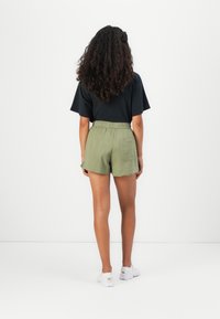 Schwarzes T-Shirt mit kurzen Ärmeln, kombiniert mit hellgrünen Leinen-Shorts mit einem elastischen Bund und Seitentaschen. Weiße Sneakers.