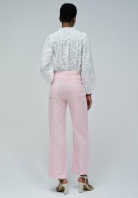 Blusa de encaje floral blanca, pantalones de lino rosa de pierna ancha y sandalias de tacón alto beige, mostrando textura y un ajuste a medida.