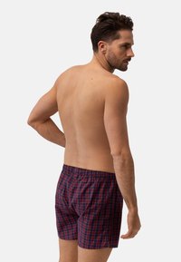 Granatowe i czerwone w kratkę bokserki z elastycznym pasem, widziane z tyłu na modelu męskim o jasnej karnacji i krótkich brązowych włosach.
